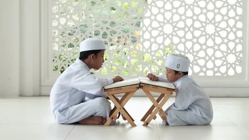 Muslim worshipper performing Salah inside a mosque with prayer mat and Quran nearby
