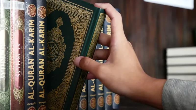 Muslim worshipper reading Quran near prayer mat at sunset in a home setting