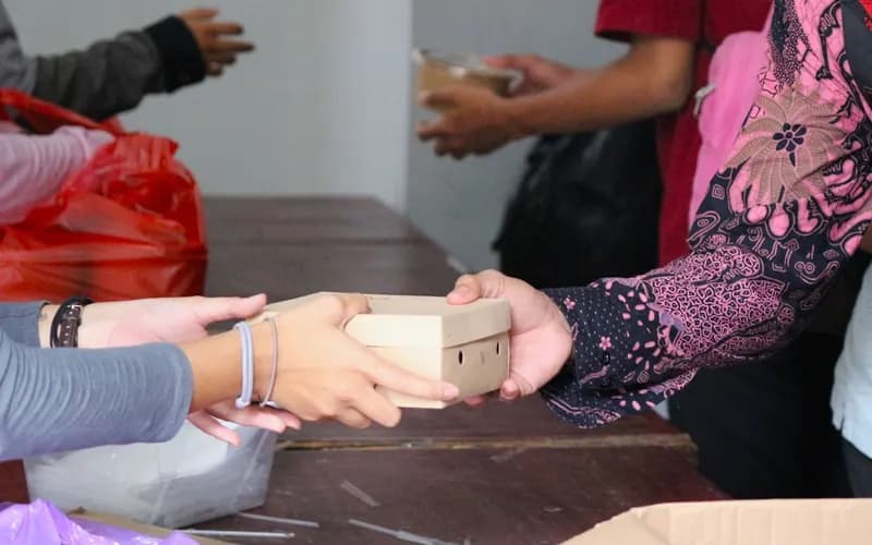 Person calculating Zakat donation amount using coins and a notebook for record keeping